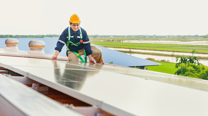 Asian male electrician engineer inspects installation of solar panels on metal roof in industrial...