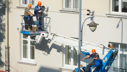 A worker in the bucket of a crane is installing lighting on the facade of the building. Renovation...