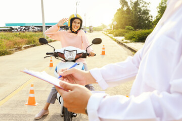 Male transport officer holds clipboard and prepares practical driving test safely in a disciplined traffic test field for young woman who is preparing to get legal motorcycle driving license.