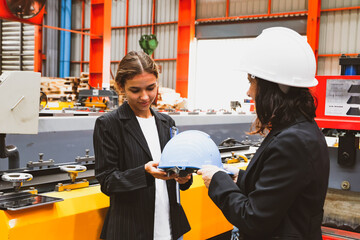 Female factory manager gladly handed over safety helmet while taking female business woman and business partner on a tour of the production work area in the metal sheet industry to ensure safety.
