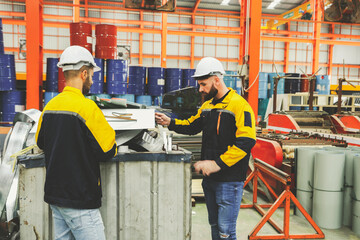 Two male workers team wearing hardhat stand sort cut metal sheets into trash bins for recycling and...
