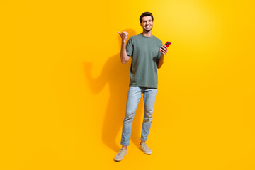 Fototapeta na wymiar Full length photo of positive funny man dressed khaki t-shirt texting modern gadget thumb empty space isolated yellow color background