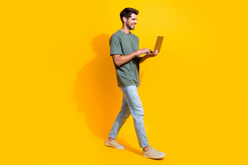 Full length photo of positive cheerful man dressed khaki t-shirt walking texting emails modern gadget isolated yellow color background