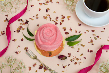 Różany deser z kawą na jasno różowym tle. W otoczeniu płatków z róży. 