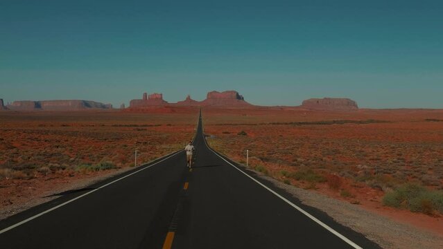 Cinematic shot of young adult man running up to camera on highway at epic sunny Forrest Gump Point desert in Arizona.