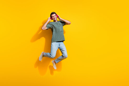 Full length photo of cheerful dreamy man dressed khaki t-shirt enjoying music earphones jumping empty space isolated yellow color background - Powered by Adobe