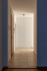 Hallway with white walls and tiles. At the end there is a closed wardrobe.