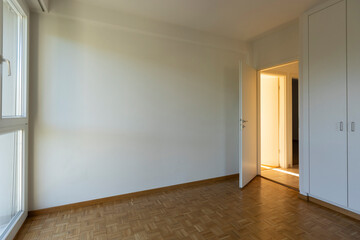 Empty room with white walls, parquet floor and a closed closet. Open door overlooking the hallway.