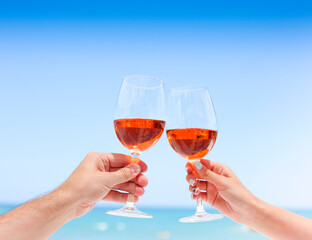 Hands of couple enjoying glasses of rose wine on tropical beach