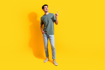 Full length photo of dreamy charming man dressed khaki t-shirt showing finger looking empty space isolated yellow color background