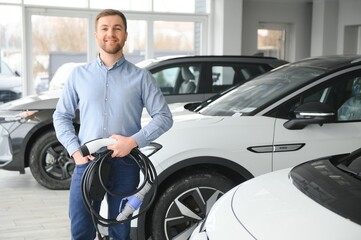 Obraz premium Young man, selling electric cars in the showroom. Concept of buying eco-friendly car for family