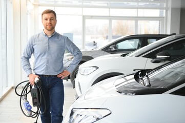 Young man buying first electric car in the showroom. Eco car sale concept
