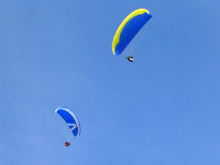 Close-up of two paragliders under a clear blue sky on a sunny day. Paragliding is an extreme sport or radical sport