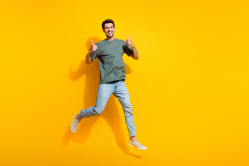 Full length photo of confident cheerful man dressed khaki t-shirt showing thumbs up jumping empty space isolated yellow color background - obrazy, fototapety, plakaty