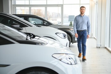 Young man buying first electric car in the showroom. Eco car sale concept