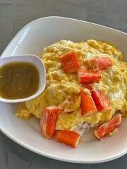 Omelette with pork bacon cutted on rice and sauce on white ceramic plate and spoon and fork.

