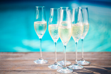 Champagne glasses on wooden background near pool