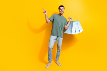 Full length photo of good mood excited man dressed khaki t-shirt rising bargains pointing empty space isolated yellow color background