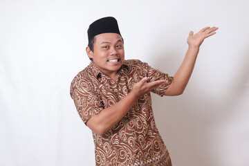 Portrait of excited Asian man wearing batik shirt and songkok smiling and looking at the camera...