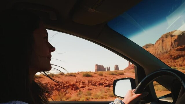Beautiful happy Caucasian woman smiling, driving along desert mountain road with window open at Monuments Valley Arizona