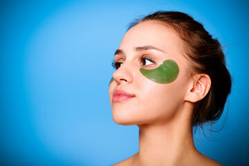 Beautiful young girl with green patches under eyes on blue background