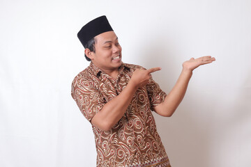 Portrait of excited Asian man wearing batik shirt and songkok smiling and looking at the camera...