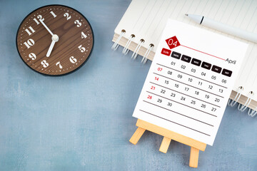 2024 April calendar page and wooden clock on wooden background.