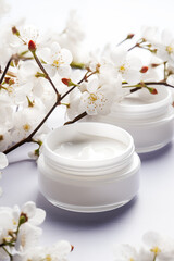 Obraz na płótnie Canvas Cosmetic cream jars mockup on white background with spring flowers. Skin care product package design.