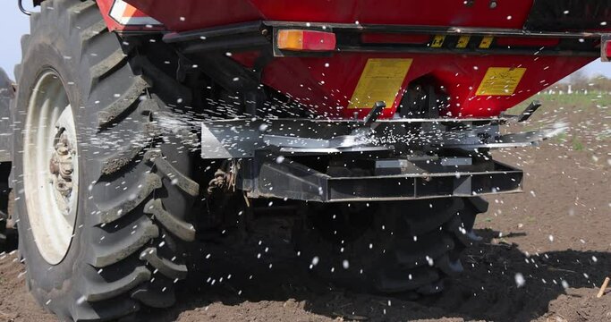 Farmer with agricultural machinery fertilizing agricultural field in spring time, slow motion. Spreading mineral fertilizer, low angle shot