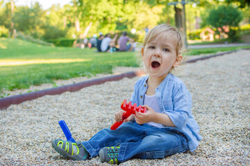 Cute little toddler boy having fun playing with colorful toys in the park, beautiful summer sunny day in children playground