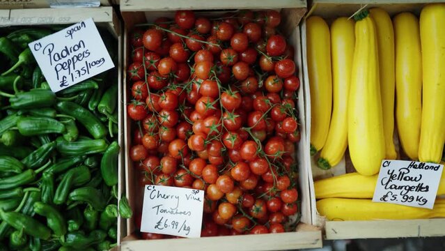 Camera pan across a vegetable shelf full of green padron peppers, cherry vine tomatoes, and yellow courgettes stored in wooden crates