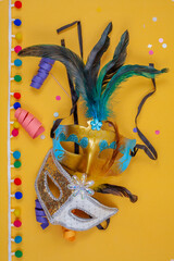 Carnival masks together adorned with feathers, colorful confetti on a vertical yellow background