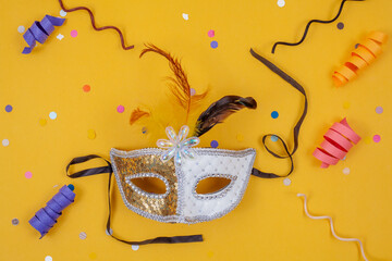 White and gold mask isolated on a yellow background decorated with colorful confetti and streamers