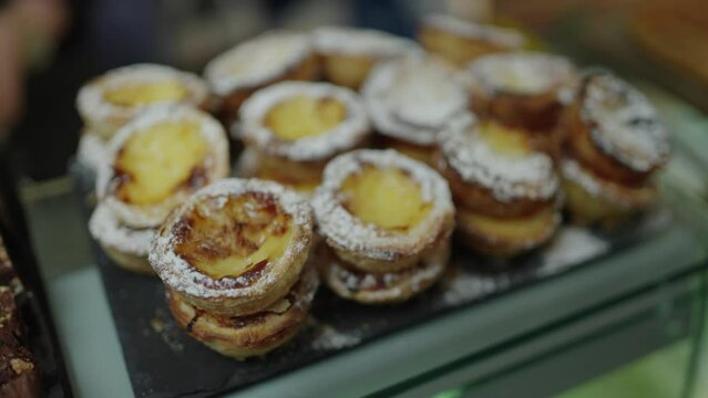 Shop Keeper places a Portuguese tart back onto a stack of tarts in a bakery