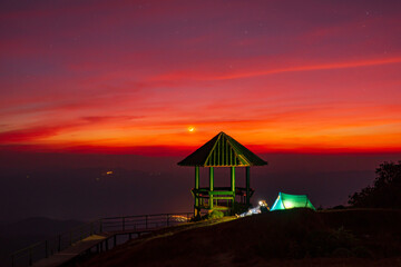 Silhouette pavilion by the hill during the dusk sky with the moon and tourists camping on the Doi Pui Co mountain in Thailand. Scenic landscape, Hiking trails, and camping in Northern Thailand