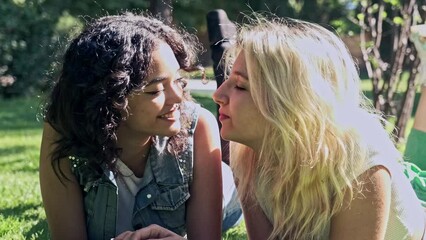 lesbian couple lying on the grass smiling talking and kissing each other on the mouth