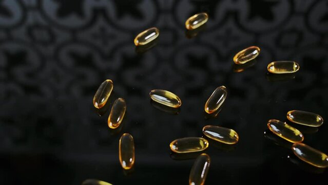 Bunch of yellow capsules pills scattered on a black surface Vitamin D3 production. Concept of taking vitamins, fish oil, bio supplements for health