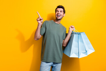 Photo of excited man dressed khaki t-shirt hold new clothes look directing at sale empty space...