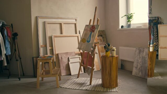 No people side footage of flower in vase painting on easel with painting tools in center of empty modern light room at home