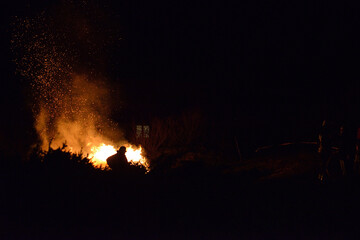Feuerwehr Mann steht in dunkler Nacht vor Lagerfeuer mit rotem Funkenflug