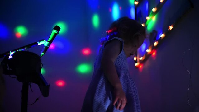 Little girl dances to the music at home with beautiful neon lights in the evening