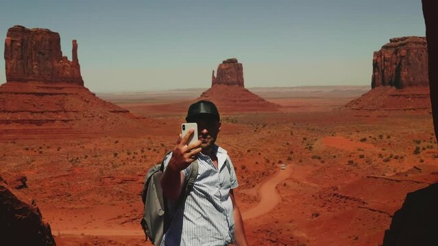 Back view young adulttourist man with backpack taking a smartphone selfie photo at epic desert vista point in Arizona.
