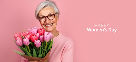 International women's day. Portrait of gorgeous gray-haired smiling grandmother with tulips in her hands on pink background. Happy pensioner, March 8, mother's day, happy birthday, spring concept