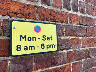 Yellow no parking at any time sign on a brick wall.