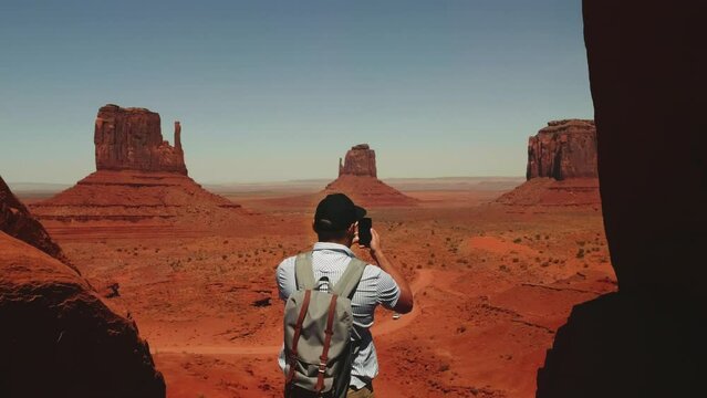 Back view young adult male tourist with backpack takes panoramic smartphone photo of breathtaking desert view in Arizona