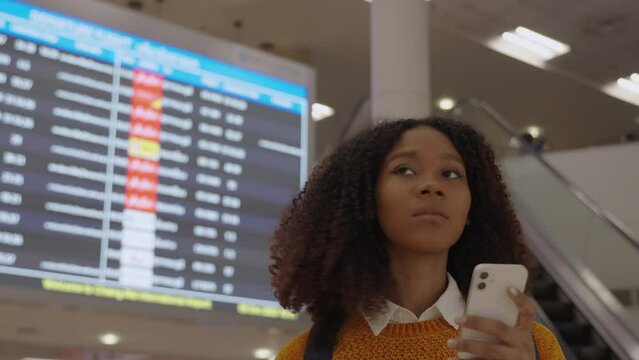 Black women with short, curly hair in the airport for a tourist trip is looking at a digital monitor screen to check the flight number, Boarding time and boarding gate number.