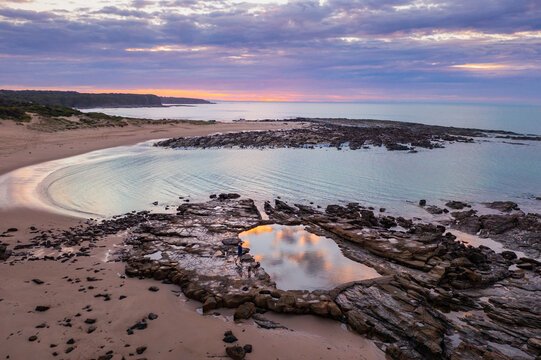 Aerial view of a bathing pool in a rocky coastline under a colourful dawn sky