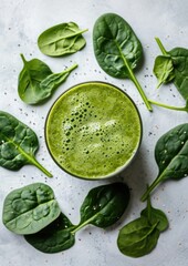 Obraz premium Fresh green smoothie next to raw spinach leaves on a white surface, concept of detox and clean eating