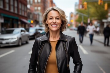 Fototapeta premium Portrait of a grinning woman in her 50s sporting a stylish leather blazer against a busy urban street. AI Generation