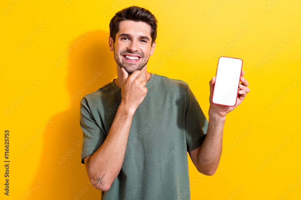 Poster Photo of minded smart man dressed khaki t-shirt show ui design on smartphone display empty space isolated on yellow color background